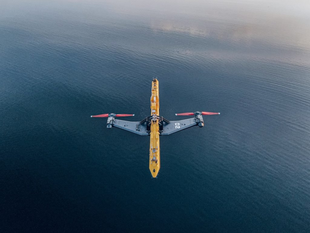 Das Bild zeigt das Gezeitenkraftwerk im Meer. An der langen, gelben Plattform sind zwei rote Turbinen zu erkennen, die seitlich ins Wasser ragen.