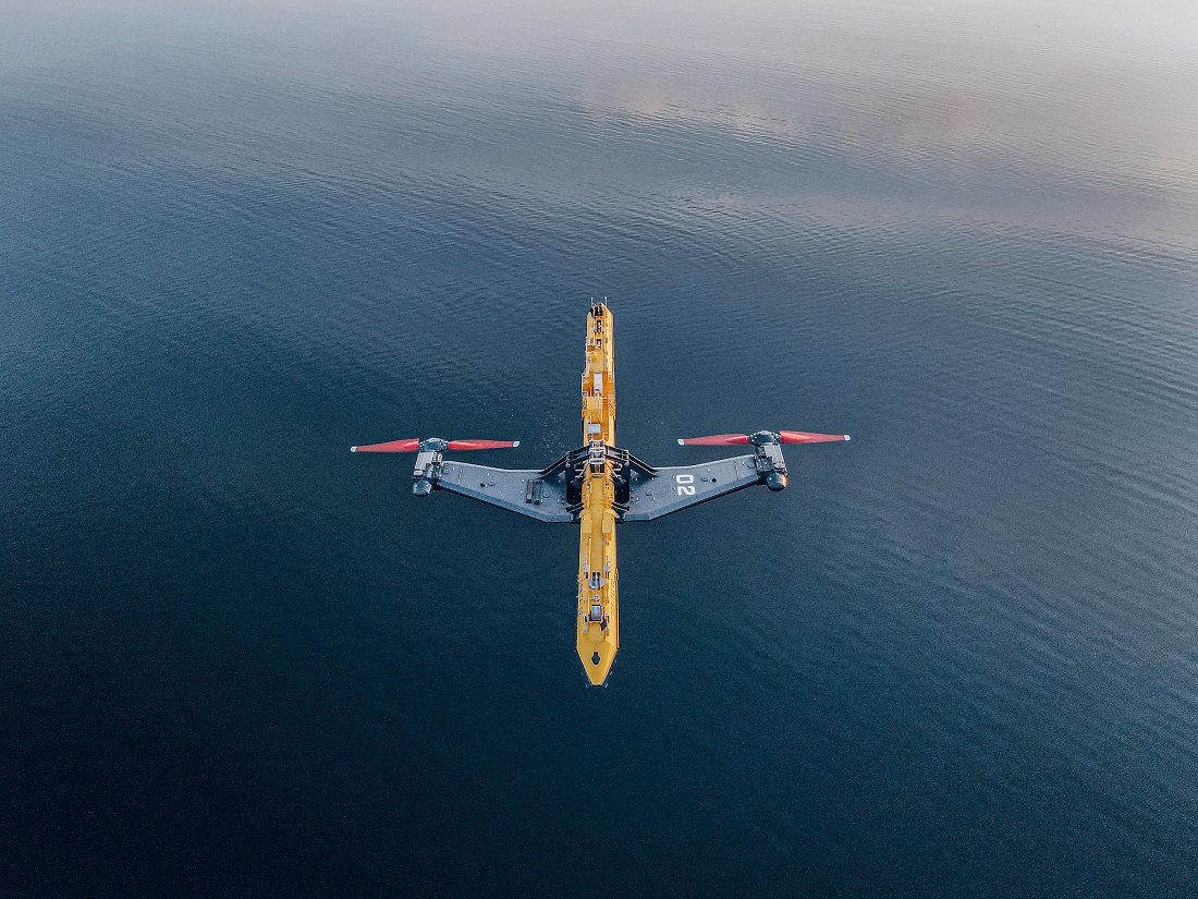 Das Bild zeigt das Gezeitenkraftwerk im Meer. An der langen, gelben Plattform sind zwei rote Turbinen zu erkennen, die seitlich ins Wasser ragen.