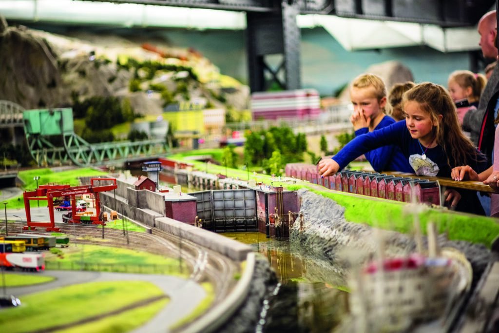 zu sehen sind Kinder die eine Modelleisenbahn anschauen.