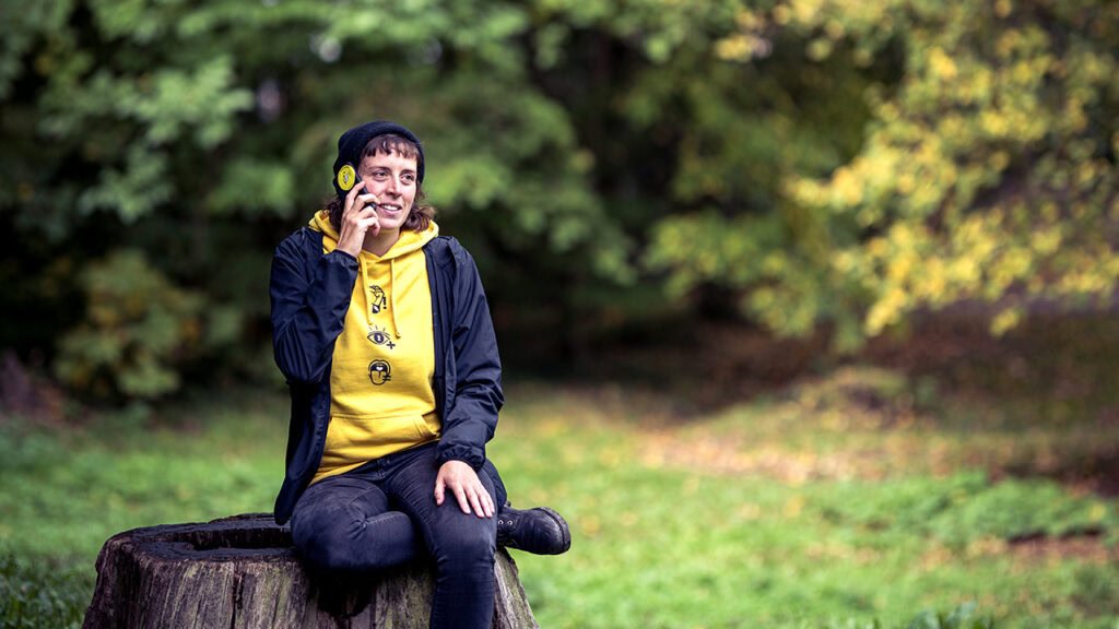 Eine Person im gelben Hoodie telefoniert im Wald.